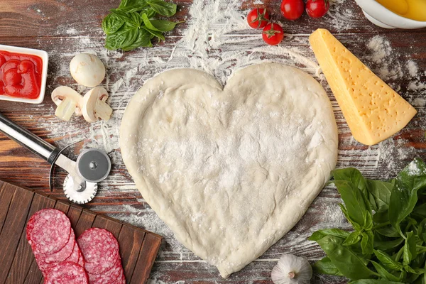 Těsto na pizzu ve tvaru srdce s přísadami na stole — Stock fotografie