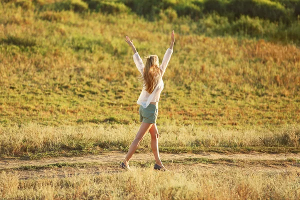Jonge vrouw lopen op de achtergrond van een veld — Stockfoto