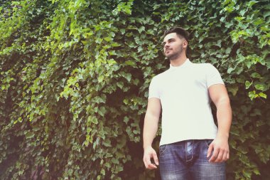 Genç adam yeşil yaprakları arka plan üzerinde boş polo gömlek