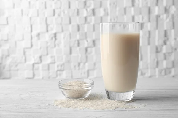 Copo de leite de arroz e tigela com grãos em mesa de madeira contra fundo branco desfocado — Fotografia de Stock