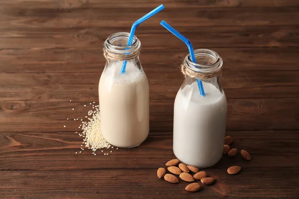 Flaskor med sesam och mandel mjölk med sugrör på träbord — Stockfoto