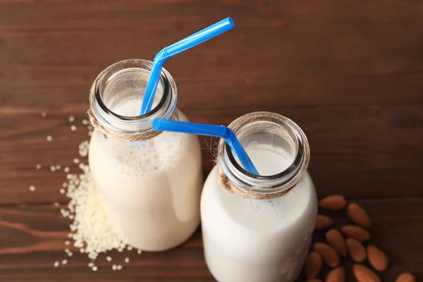 Bottles of sesame and almond milk with straws on wooden table, close up view — Stock Photo, Image