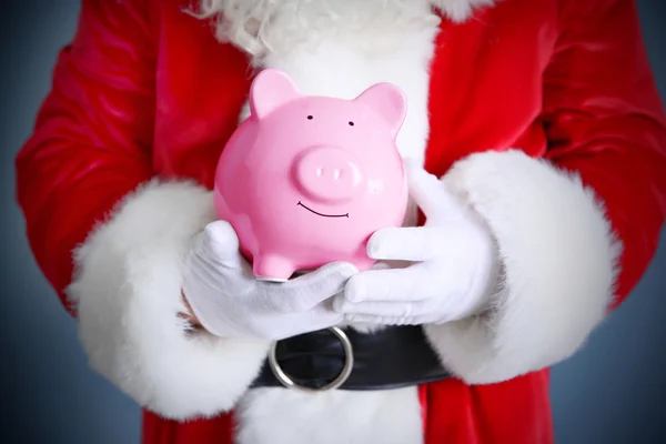 Santa Claus hands holding piggy bank on blue background — Stock Photo, Image