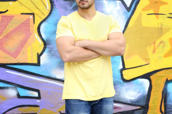 Young man in yellow t-shirt against graffiti wall, closeup