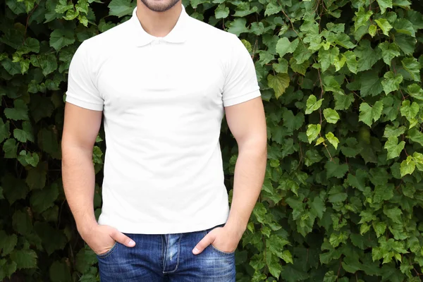 Jovem em branco camisa pólo no fundo folhas verdes, close-up — Fotografia de Stock