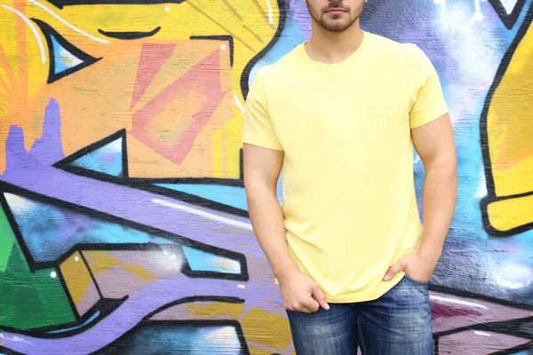 Young man in blank t-shirt against graffiti wall, closeup — ストック写真