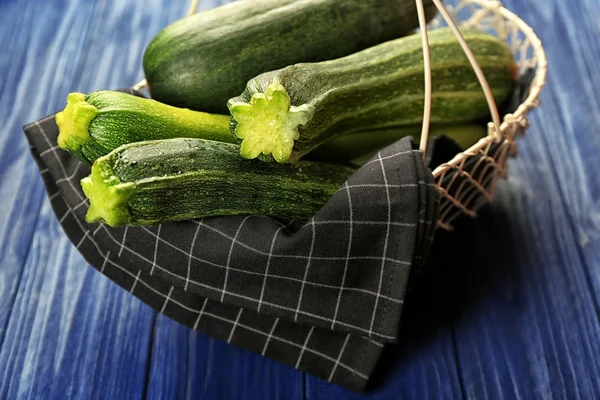 Fresh zucchini and napkin in basket on blue wooden background — Stock Photo, Image