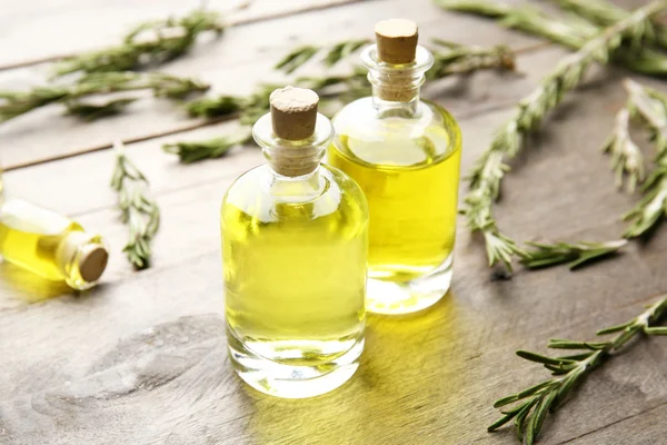 Bottles of coniferous essential oil and rosemary branches on wooden background, close up view — Stock Photo, Image