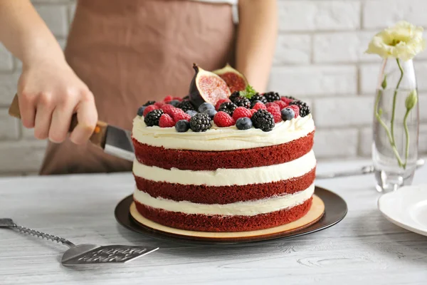 Woman cutting tasty cake with berries on kitchen — Stock Photo, Image