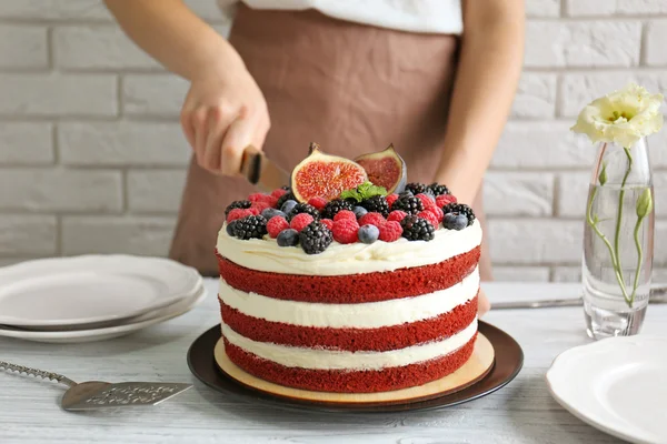 Mujer cortando sabroso pastel con bayas en la cocina —  Fotos de Stock