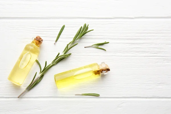 Flaschen mit ätherischem Nadelöl und Rosmarinzweig auf Holzgrund, Nahaufnahme — Stockfoto