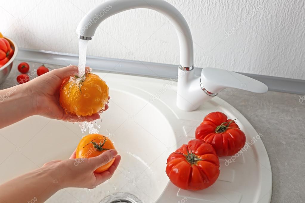 Female hands washing tomatoes in kitchen sink