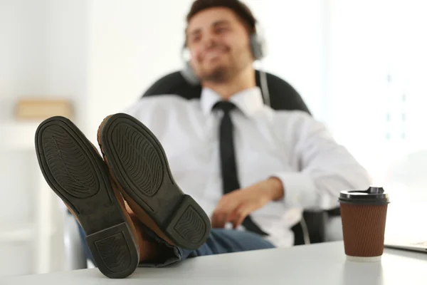 Hombre guapo escuchando música con auriculares y poniendo los pies en la mesa — Foto de Stock