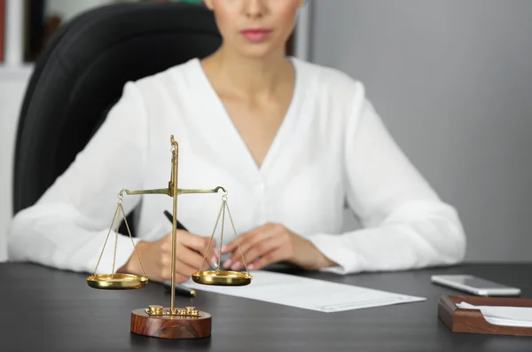 Весы правосудия и деловая женщина, сидящая за столом — стоковое фото