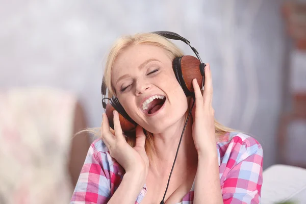 Charming blonde girl with headphones listening to music and singing in the room — Φωτογραφία Αρχείου