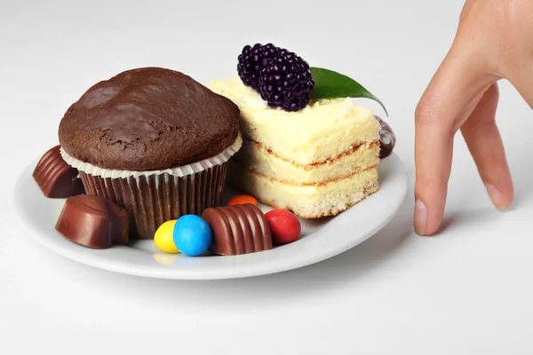 Tangan dan piring wanita dengan kue spons lezat, muffin coklat dan permen di atas meja putih. Konsep interupsi diet — Stok Foto