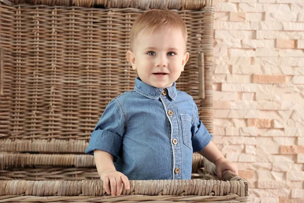 Menino elegante em camisa jeans em uma cesta de vime em um fundo de parede de pedra. Conceito de moda — Fotografia de Stock