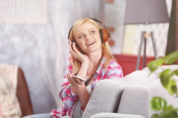 Vrolijk meisje met hoofdtelefoon en de telefoon luisteren naar muziek thuis — Stockfoto