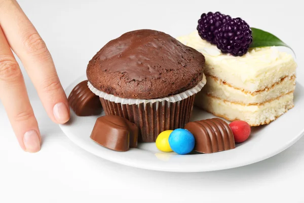 Mano y plato femenino con sabroso bizcocho, magdalena de chocolate y dulces sobre mesa blanca. Concepto de interrupción de la dieta —  Fotos de Stock