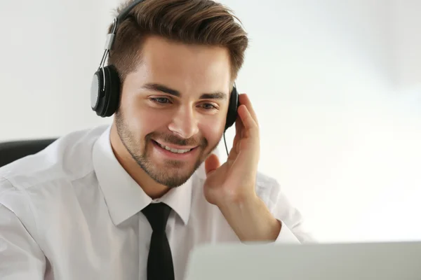 Joven guapo escuchando música con auriculares y trabajando en el ordenador portátil en la oficina — Foto de Stock