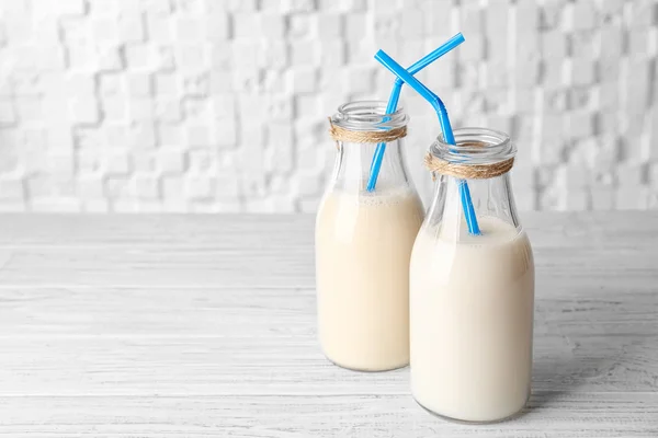 Дві пляшки смачного молока з сосками на дерев'яному столі на білому розмитому фоні — стокове фото
