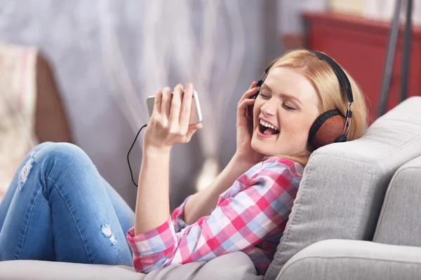 Vrolijk meisje met hoofdtelefoon en de telefoon luisteren naar muziek thuis — Stockfoto