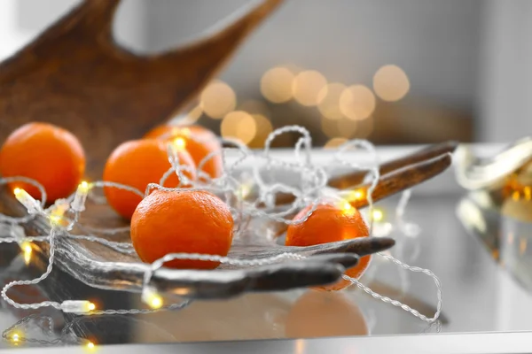 Mandarins com luzes guirlanda na mesa em quarto decorado — Fotografia de Stock