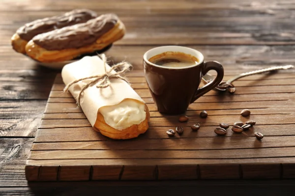 Tasty eclair and cup of coffee on wooden background — Stock Photo, Image