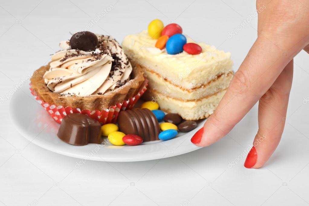 Female hand and plate with tasty cakes and sweets on white table. Diet interruption concept
