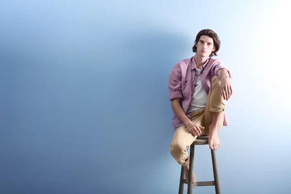 Csinos fiatal ember ül a széken a kék háttér — Stock Fotó