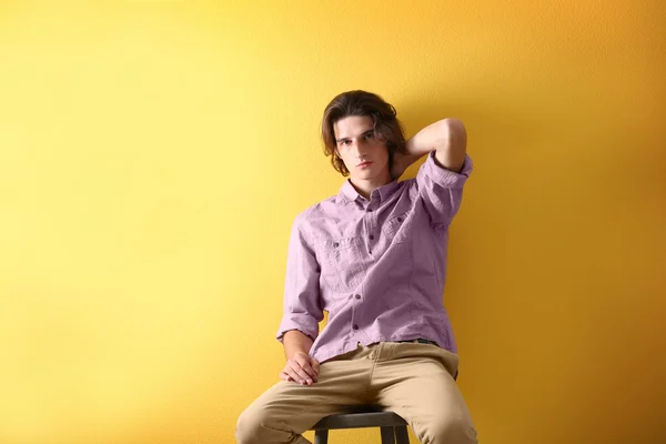 Handsome young man sitting on stool on yellow background — Stock Photo, Image