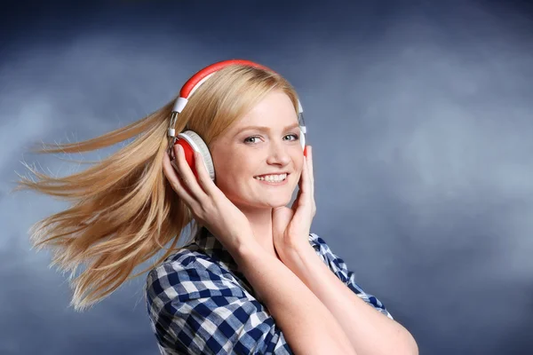 Menina loira bonita com fones de ouvido em um fundo embaçado cinza — Fotografia de Stock