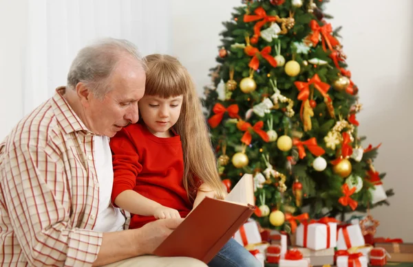 Uomo anziano leggere libro con sua nipote in soggiorno decorato per Natale — Foto Stock
