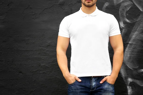 Young man in blank polo shirt against graffiti wall, closeup — Stock Photo, Image