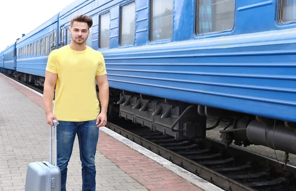 Jovem de t-shirt em branco em pé na plataforma ferroviária com mala — Fotografia de Stock