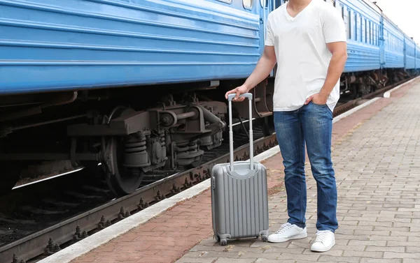 Jonge man in lege t-shirt met koffer staande op het platform van de spoorwegen in de buurt van trein, close-up — Stockfoto