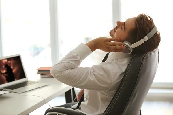 Pohledný mladý muž poslouchá hudbu se sluchátky v kanceláři — Stock fotografie