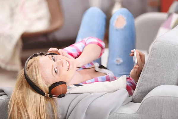 Charmante fille blonde avec écouteurs écoutant de la musique et couchée sur le canapé — Photo