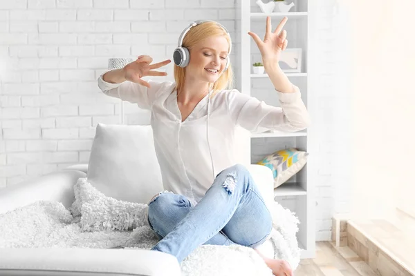 Mujer joven con auriculares disfrutando de música favorita y sentada en el sofá —  Fotos de Stock