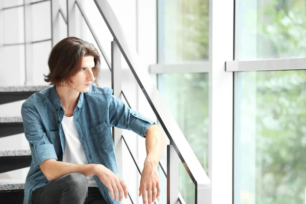 Knappe jonge man zit op de trappen op lichte achtergrond — Stockfoto