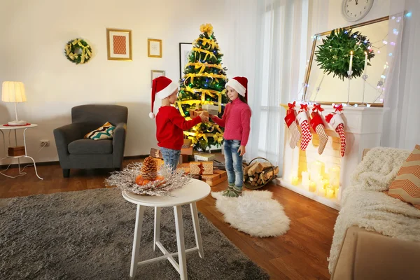 Lindos niños pequeños en sombreros de Santa con regalos de Navidad en casa —  Fotos de Stock