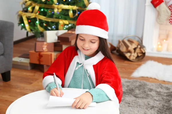 Милая маленькая девочка пишет письмо Санта-Клаусу за столом — стоковое фото