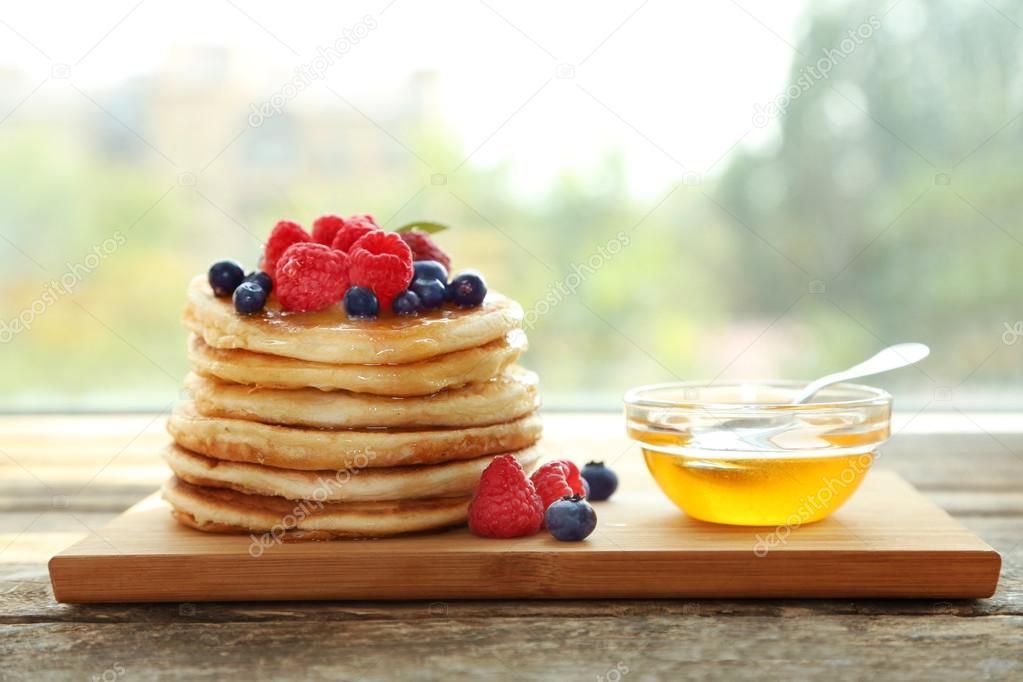 Stack of pancakes and bowl with honey on wooden kitchen board