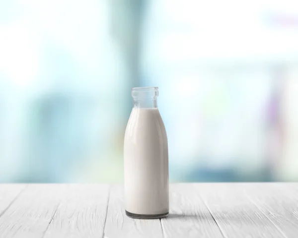 Glass bottle of milk on white wooden table against blurred background. Dairy concept. — Stock fotografie