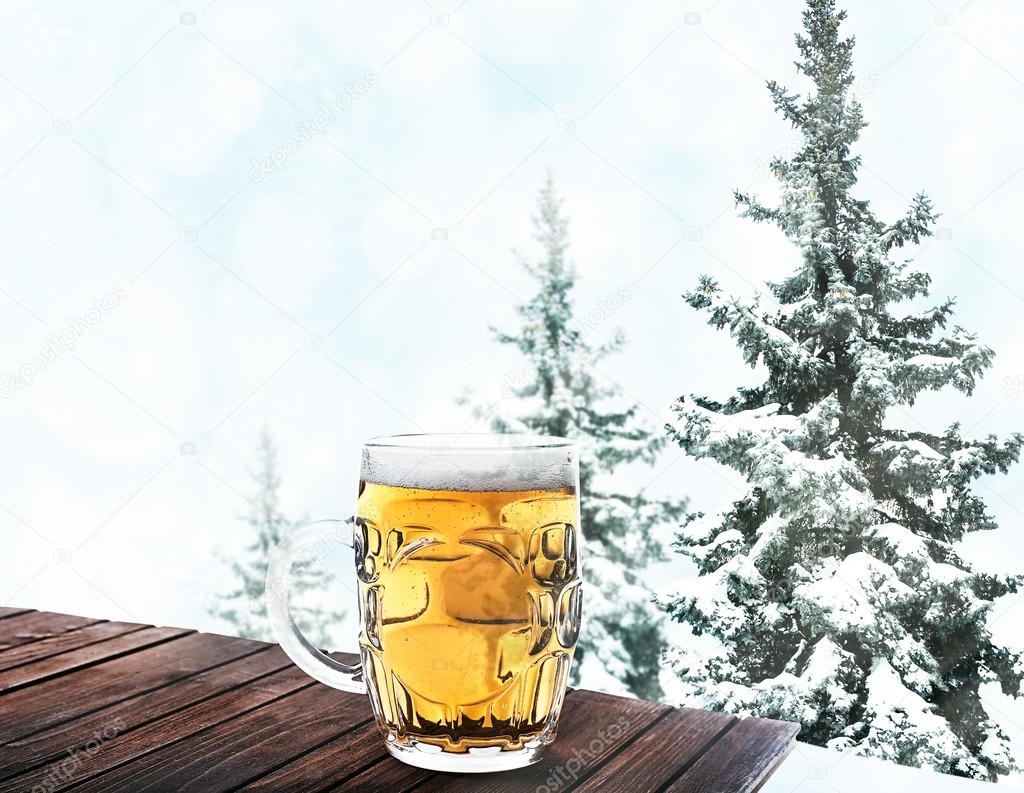 Glass of beer on wooden table against winter nature background.