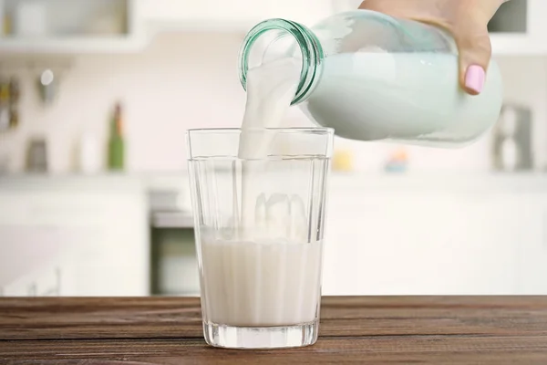 Female hand pouring milk into glass against blurred kitchen background. Dairy concept. — ストック写真