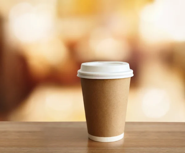 Paper cup of coffee on wooden table against blurred background. — Stock Photo, Image