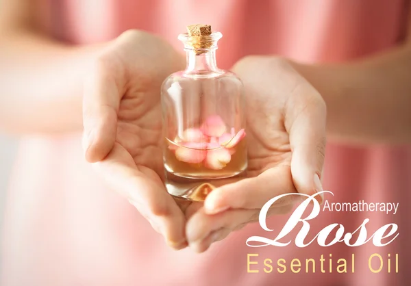 Vrouwelijke hand met glazen fles van essentie, close-up. Tekst Rose etherische olie op achtergrond. Spa beauty concept. — Stockfoto