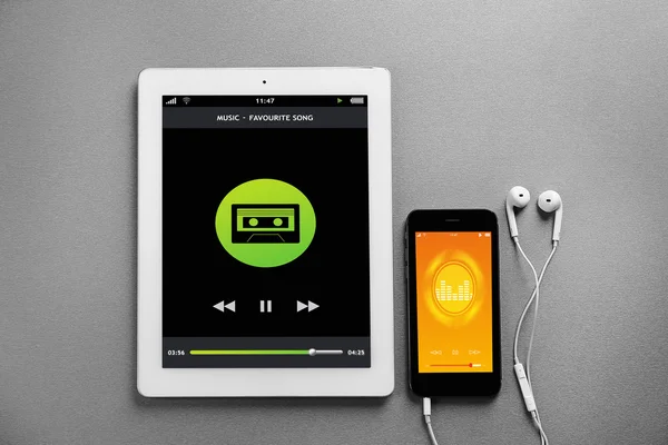 Tablet, akıllı telefon ve kulaklık gri arka plan üzerinde. Müzik çalar arayüzü ekranda.