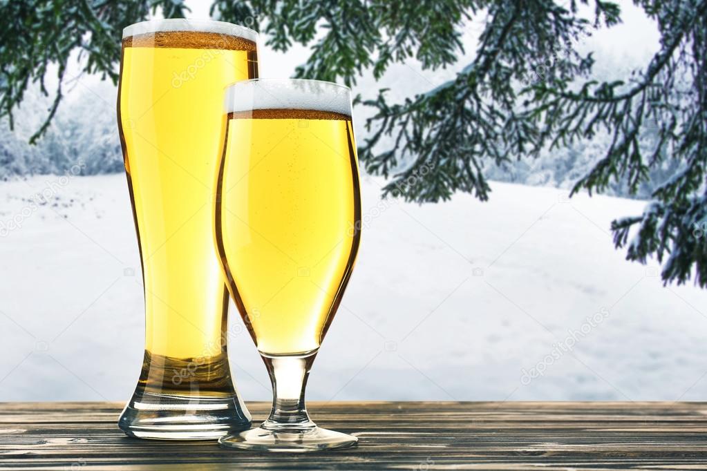 Glasses of beer on wooden table against winter nature background.